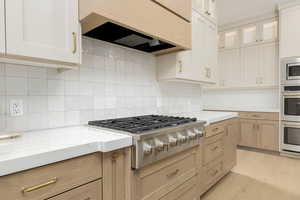 Kitchen featuring premium range hood, decorative backsplash, appliances with stainless steel finishes, light wood-style flooring, and glass insert cabinets