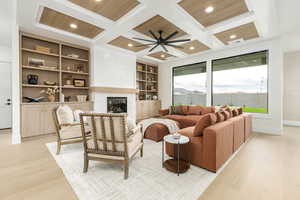 Living room with a glass covered fireplace, beamed ceiling, light wood-style floors, built in features, and coffered ceiling
