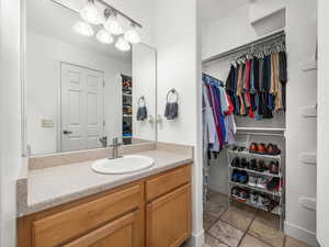 Bathroom with a walk in closet, vanity, and stone tile floors