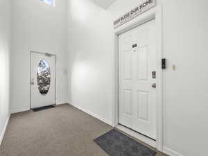 Carpeted entryway with baseboards and a towering ceiling