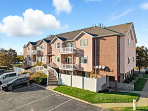 View of front of property with uncovered parking, brick siding, and a balcony