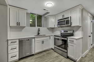 Kitchen featuring stainless steel appliances, white cabinetry, backsplash, and light wood finished floors