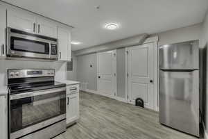 Kitchen with appliances with stainless steel finishes, white cabinetry, light wood-style flooring, and decorative backsplash
