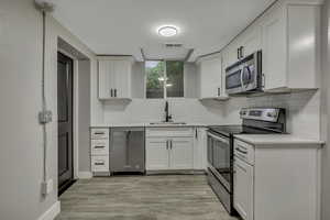 Kitchen with appliances with stainless steel finishes, white cabinetry, tasteful backsplash, light wood-type flooring, and light stone countertops