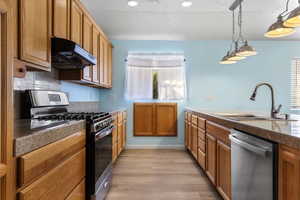 Kitchen with stainless steel appliances, brown cabinetry, under cabinet range hood, light wood-style floors, and a textured ceiling