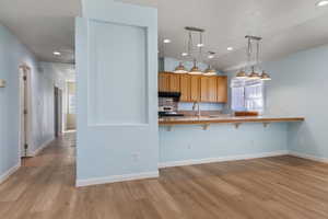 Kitchen with light wood-style flooring, pendant lighting, a kitchen breakfast bar, light countertops, and recessed lighting