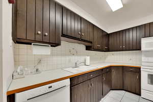 Kitchen featuring dark brown cabinets, white appliances, decorative backsplash, light countertops, and light tile patterned floors