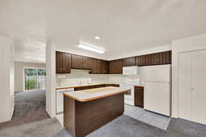 Kitchen with dark brown cabinets, white appliances, light countertops, a kitchen island, and recessed lighting