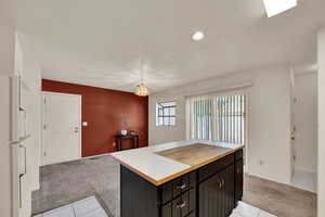 Kitchen featuring light carpet, freestanding refrigerator, a kitchen island, light tile patterned floors, and dark cabinetry