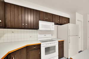 Kitchen with dark brown cabinetry, white appliances, light countertops, and tasteful backsplash