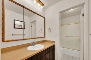 Full bathroom with a textured ceiling, enclosed tub / shower combo, light tile patterned floors, and vanity