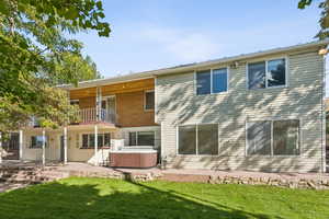Rear view of house featuring a hot tub, a patio, a balcony, and a lawn