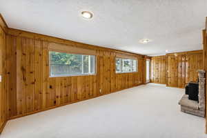 Unfurnished living room featuring a wood stove, a textured ceiling, carpet, and wood walls