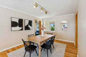 Dining area with rail lighting, ornamental molding, a textured ceiling, and light wood-style floors