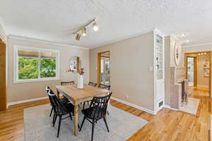 Dining area with ornamental molding, plenty of natural light, light wood-style flooring, rail lighting, and a textured ceiling