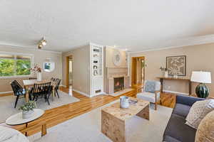 Living area featuring wood finished floors, a tiled fireplace, ornamental molding, and a textured ceiling