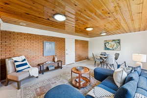 Living room featuring brick wall, carpet floors, wood ceiling, and ornamental molding