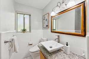 Half bathroom featuring vanity, tile walls, and a wainscoted wall