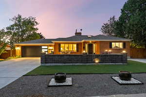 View of front of home featuring a fire pit, brick siding, driveway, a chimney, and a patio area