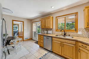 Kitchen featuring backsplash, appliances with stainless steel finishes, light stone counters, and light tile patterned flooring