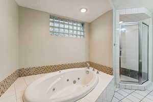 Full bath featuring a shower stall, light tile patterned floors, a tub with jets, and lofted ceiling