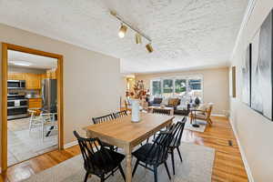 Dining area with track lighting, ornamental molding, light wood finished floors, and a textured ceiling