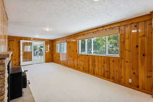 Unfurnished living room featuring wood walls, light colored carpet, and a textured ceiling