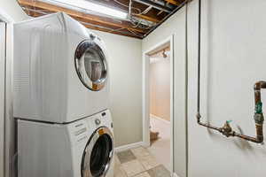 Laundry area featuring light tile patterned flooring, stacked washer / drying machine, and light colored carpet