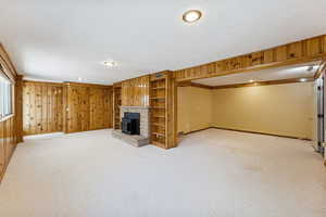 Unfurnished living room featuring carpet, wood walls, a stone fireplace, a textured ceiling, and recessed lighting