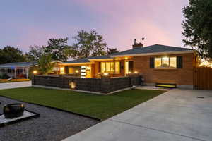 View of front of home featuring brick siding, a chimney, a patio area, and concrete driveway