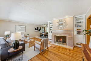 Living room with built in features, a tile fireplace, light wood-style flooring, a textured ceiling, and ornamental molding