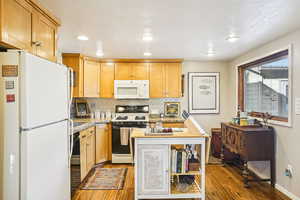 Kitchen featuring white appliances, backsplash, light wood-type flooring, recessed lighting, and light stone countertops