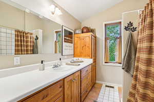 Full bath with vanity, light tile patterned flooring, vaulted ceiling, and a shower with curtain