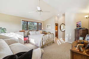 Carpeted bedroom featuring high vaulted ceiling, ceiling fan, and ensuite bathroom