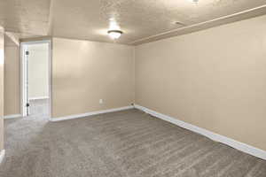 Carpeted spare room with a textured ceiling and baseboards