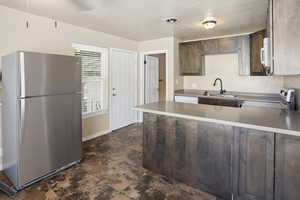 Kitchen with white appliances, a peninsula, a textured ceiling, dark brown cabinets, and dark stone finish floors