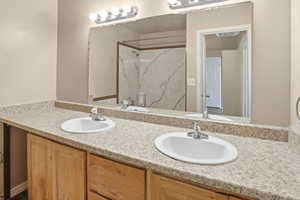 Full bathroom featuring double vanity and a marble finish shower