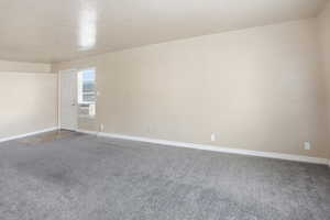 Carpeted spare room with a textured ceiling and baseboards