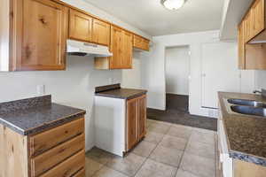 Kitchen featuring under cabinet range hood, dark countertops, and light tile patterned floors