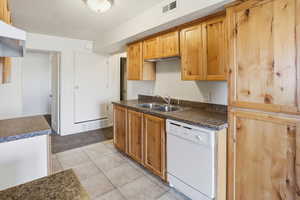 Kitchen with white dishwasher, dark countertops, light tile patterned floors, and brown cabinets