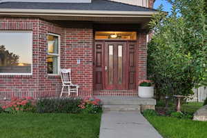 Entrance to property featuring brick siding, a porch, roof with shingles, and a yard