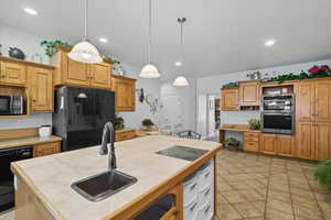 Kitchen featuring an island with sink, black appliances, open shelves, pendant lighting, and light tile patterned floors
