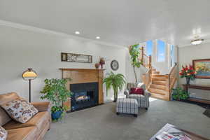 Carpeted living room with ornamental molding, a fireplace, stairway, and recessed lighting