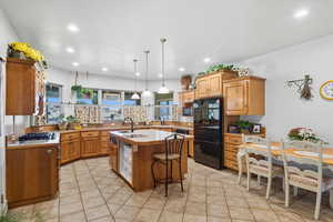 Kitchen with light countertops, a kitchen breakfast bar, brown cabinetry, an island with sink, and freestanding refrigerator