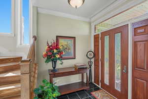 Foyer entrance with crown molding, stairs, and dark tile patterned flooring