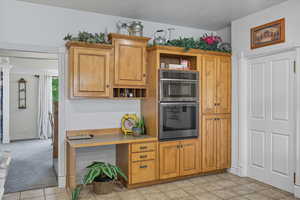 Kitchen featuring open shelves, stainless steel double oven, brown cabinets, light tile patterned floors, and light carpet