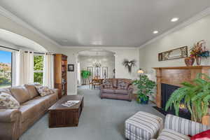 Carpeted living area with arched walkways, ornamental molding, ornate columns, a fireplace with flush hearth, and recessed lighting