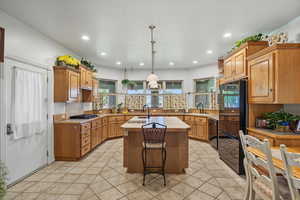 Kitchen with a kitchen island with sink, brown cabinetry, hanging light fixtures, tile countertops, and black appliances