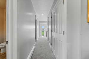 Corridor featuring light colored carpet and a textured ceiling