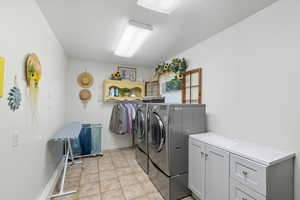 Laundry area featuring light tile patterned floors, washing machine and dryer, and cabinet space